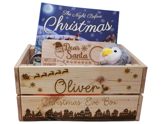 A picture of the engraved box, with the Name Oliver on it and christmas eve box below, below the words is a picture of a nativity village and in the box are a book, a toy penguin and a christmas tray. 